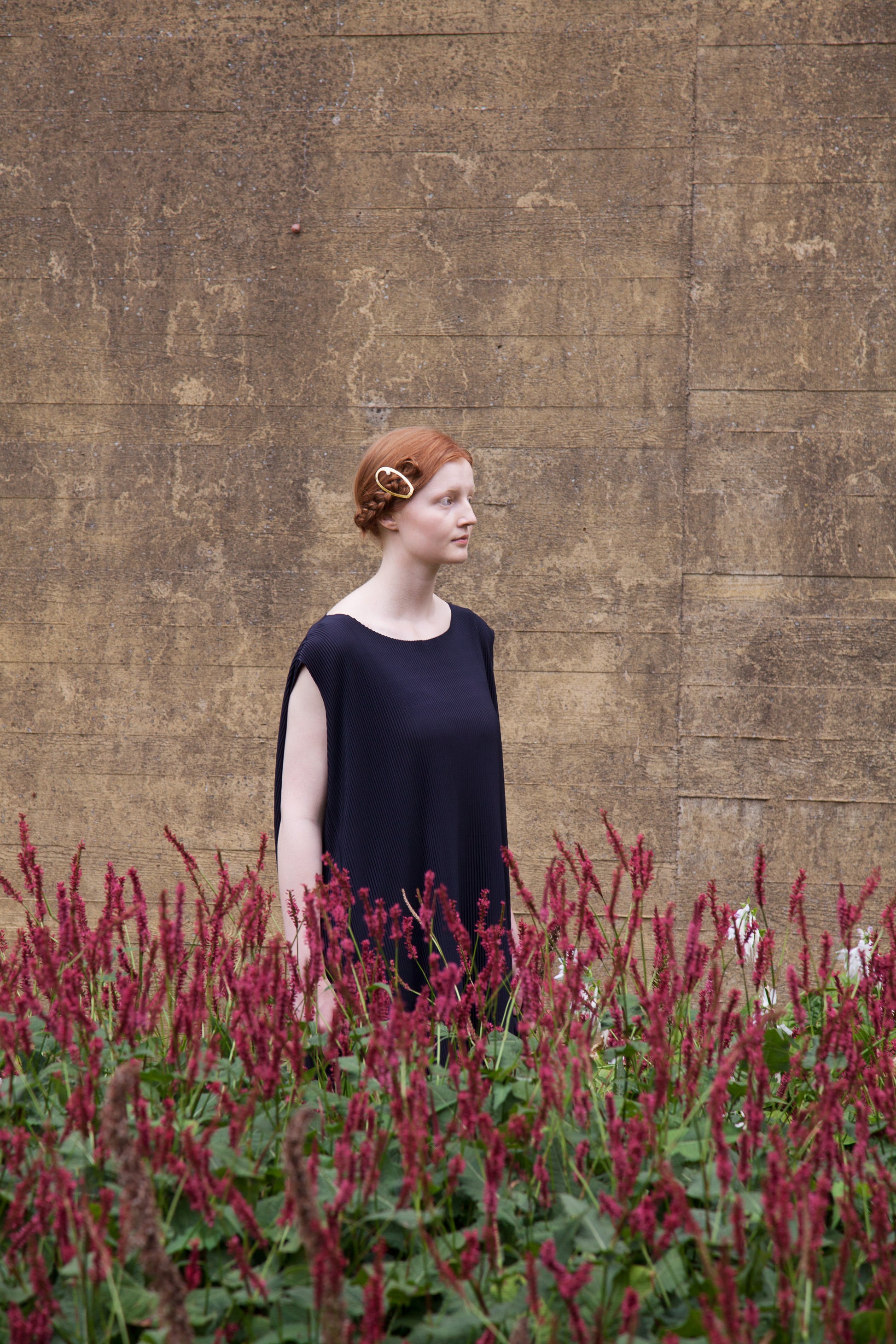 Model standing in a flower bed wearing her hair in a braided side knot accessorized with designer hair clip ELSA by Clinq
