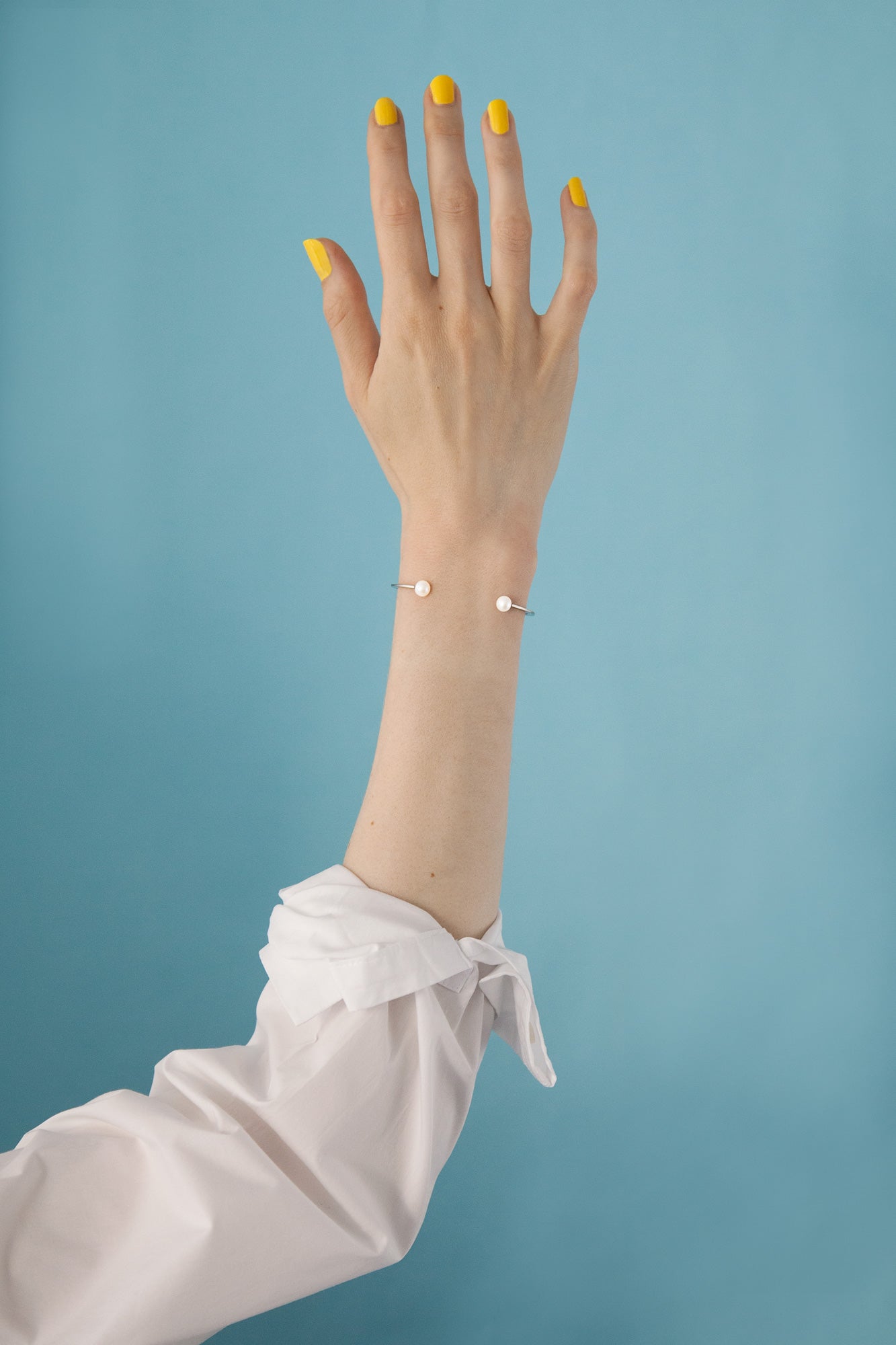 Model wearing the designer cuff bracelet Della by Clinq accented with pearls and yellow nail polish