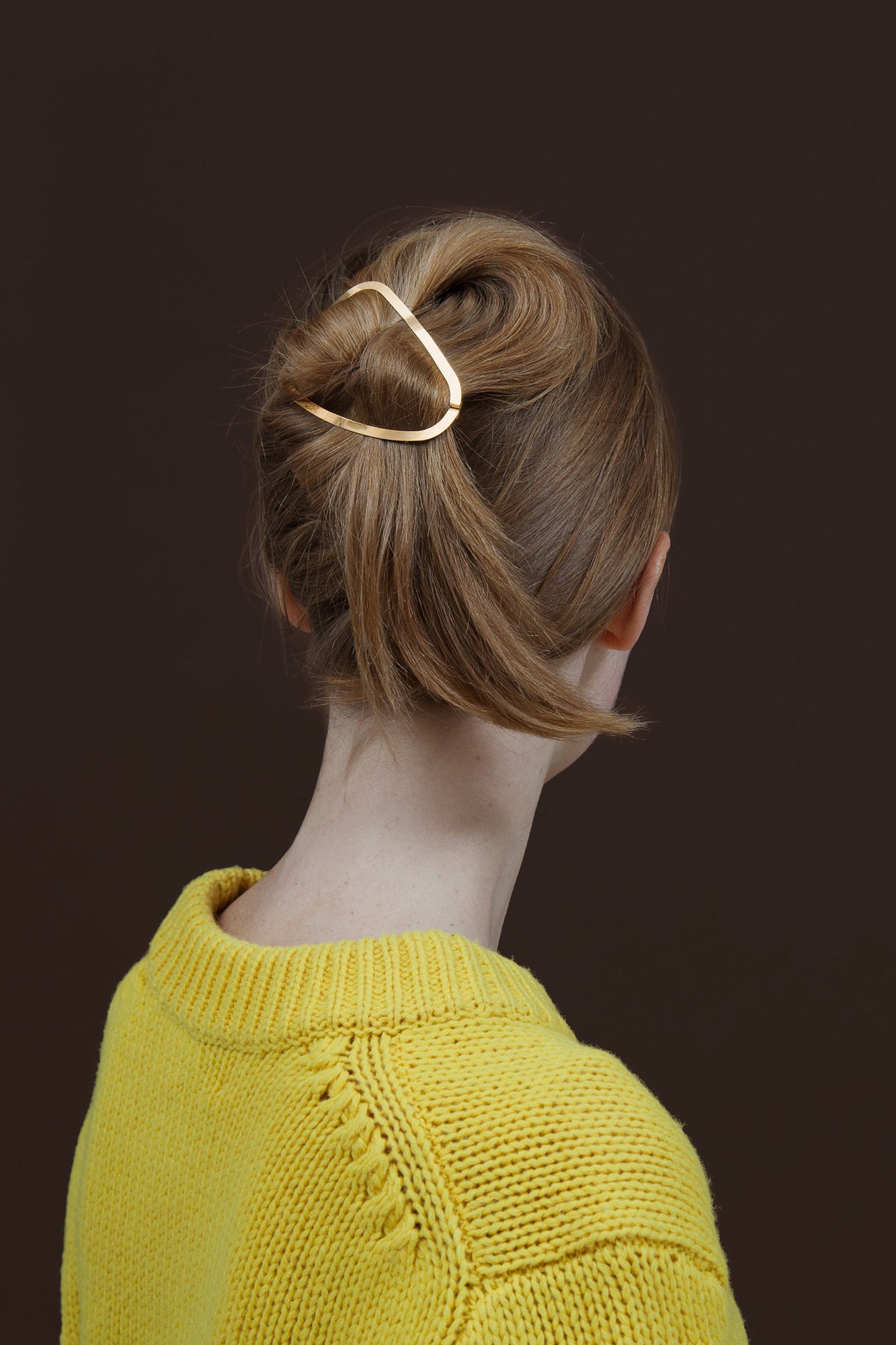 Back view of model wearing her hair in a twisted top knot secured with designer hair clip Elissa in gold-plated by Clinq 