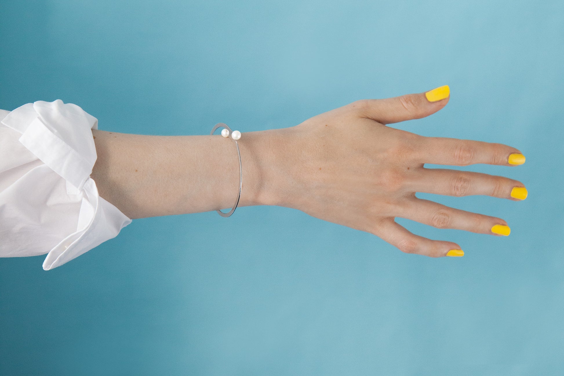 Close up of the Designer bangle bracelet April by CLINQ. Mirror polished stainless steel with cultured freshwater pearls. Available in Silver-tone and Gold-plated . Handcrafted jewelry made in Berlin