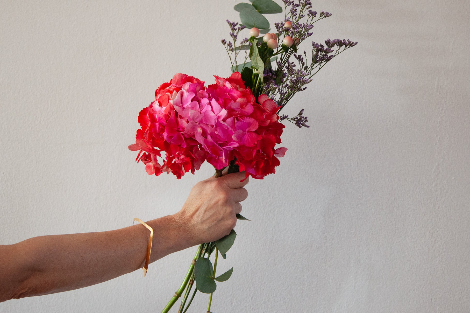Arm featuring the abstract heart shape bangle Zeta holding a bouquet of pink flowers 