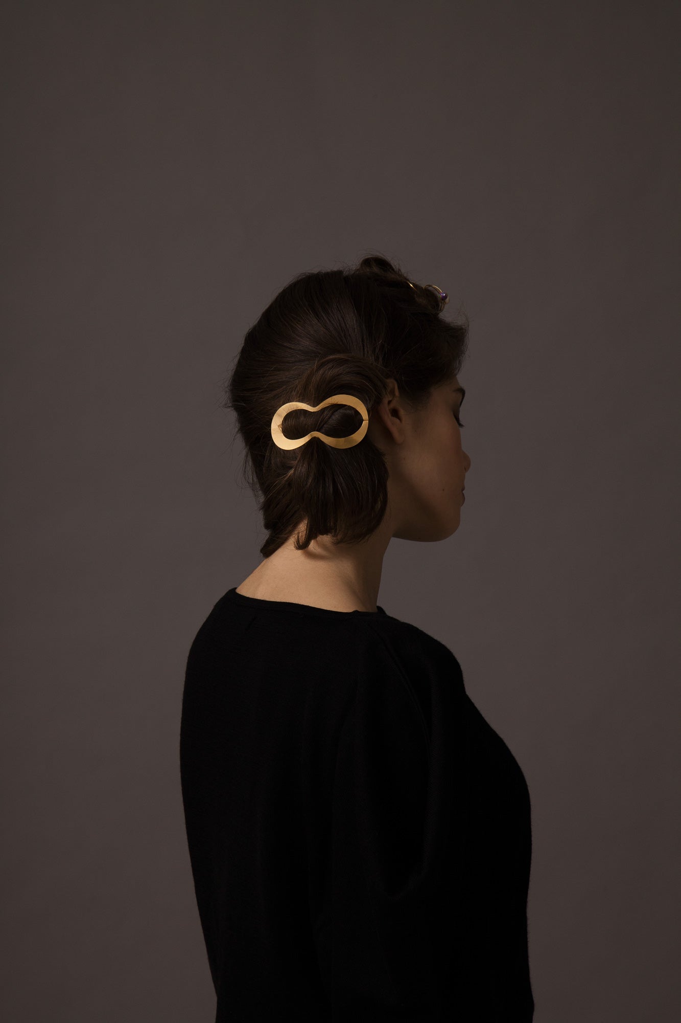 Side view of model with low messy side bun secured with the designer hair clip CLIO by CLINQ in Gold-plated