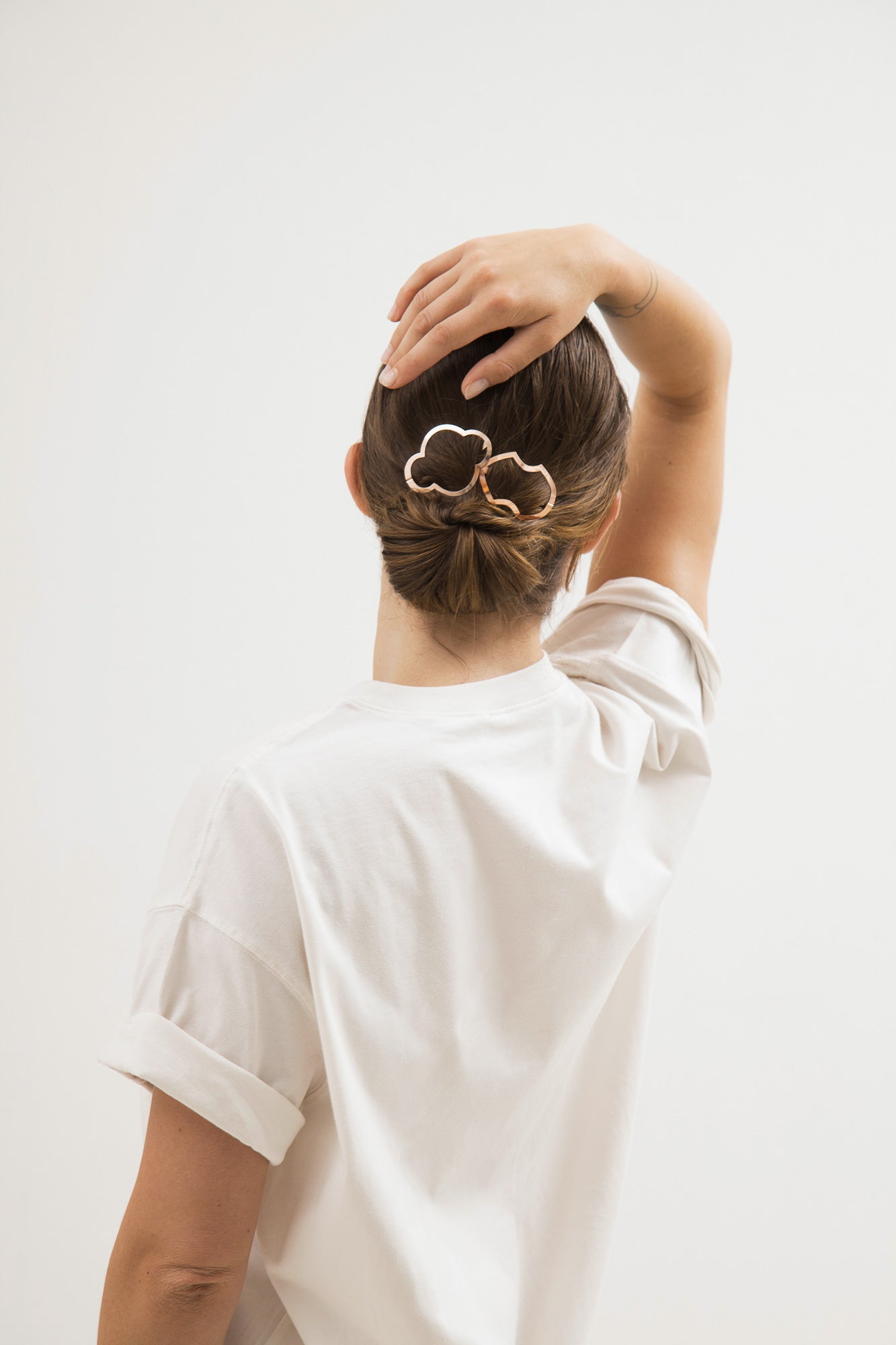 Model wears a neat low bun accented with CLINQ designer hair clips Nona and Alisa.