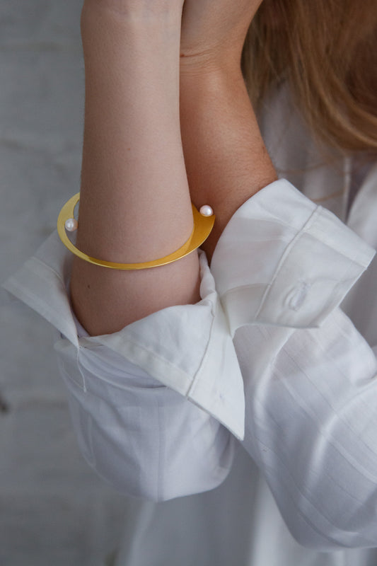 Close up of model wearing minimalist designer bangle bracelet Elea by Clinq in gold-plated with freshwater pearls 