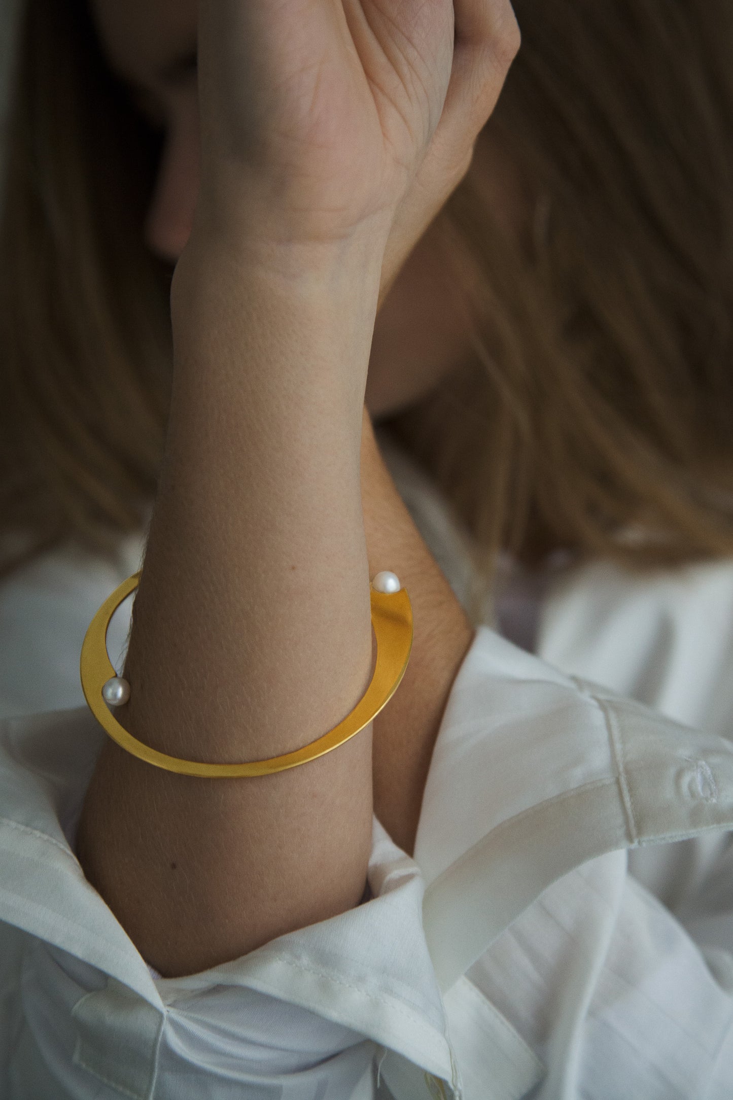 Close-up of a model wearing a white shirt styled with the designer bangle bracelet ELEA by CLINQ