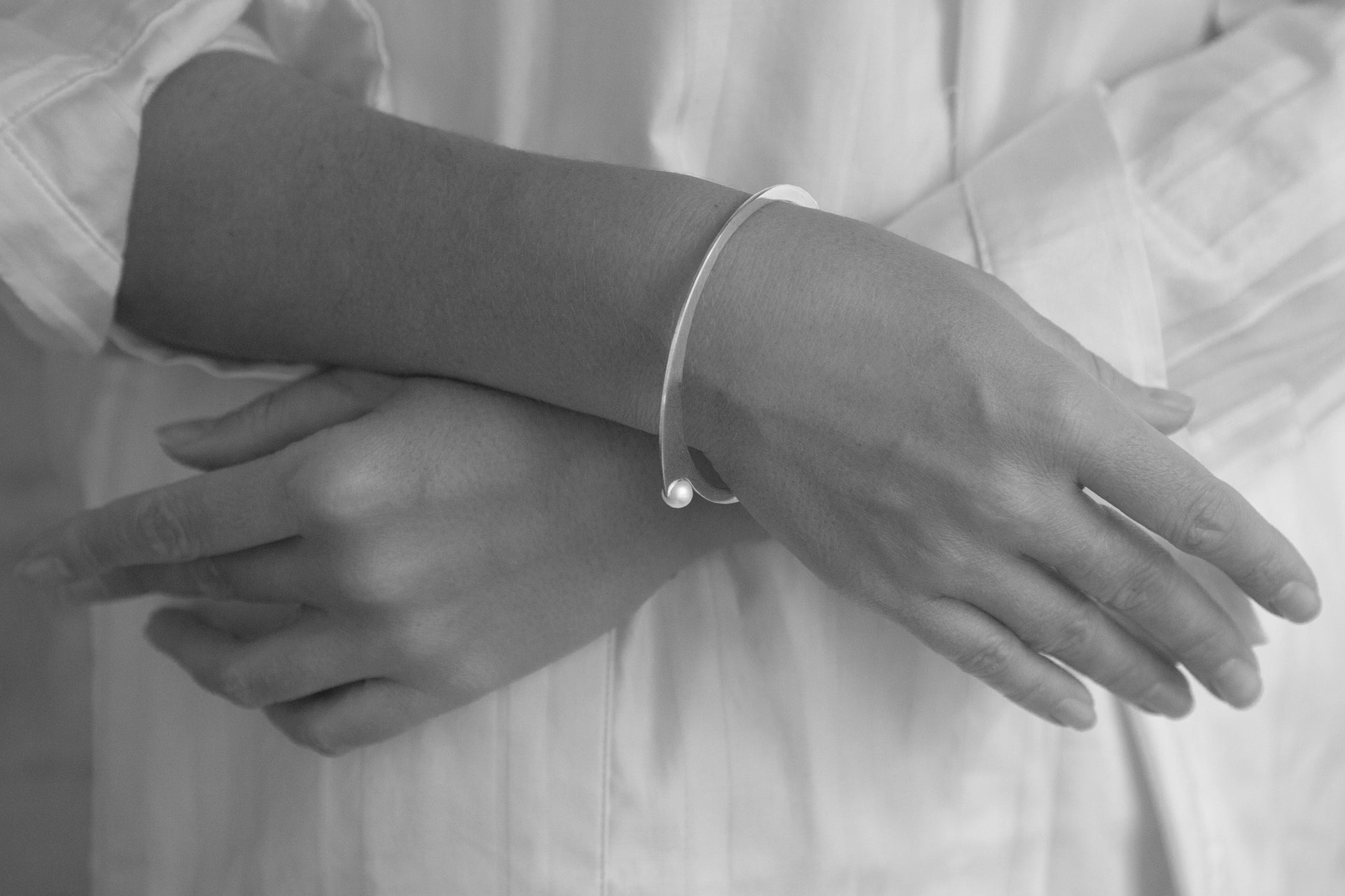 Model crossing her arms showing the designer bangle bracelet ELEA by CLINQ gold-plated with freshwater pearls